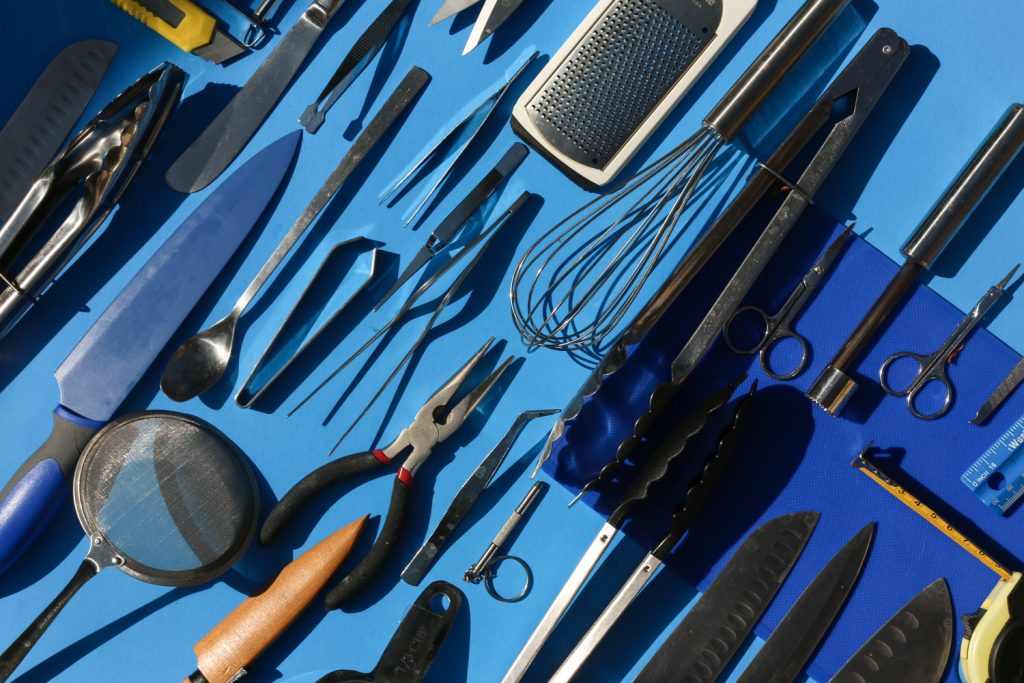 A selection of professional food styling equipment including knives, whisks, tongs and sifters